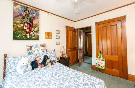 Photo of a woman's bedroom. The camera is facing the doorway into the room. There are two doors on either side, one leads to the bathroom, the other a large closet. On the bed is an assortment of stuffed animals and a 